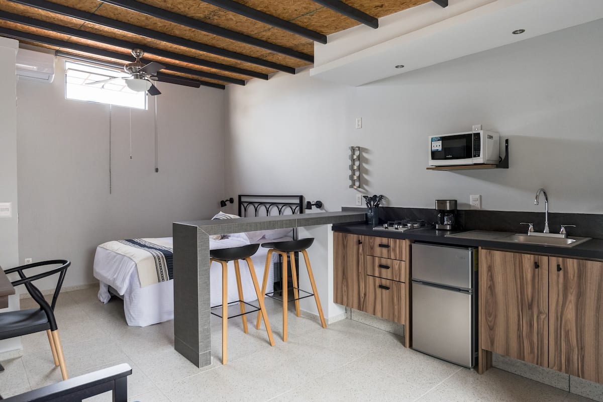 A compact kitchen with a built-in refrigerator, a microwave, and a coffee maker. There is a small dining area with a table and two bar stools. The kitchen features wooden cabinets and a black countertop.