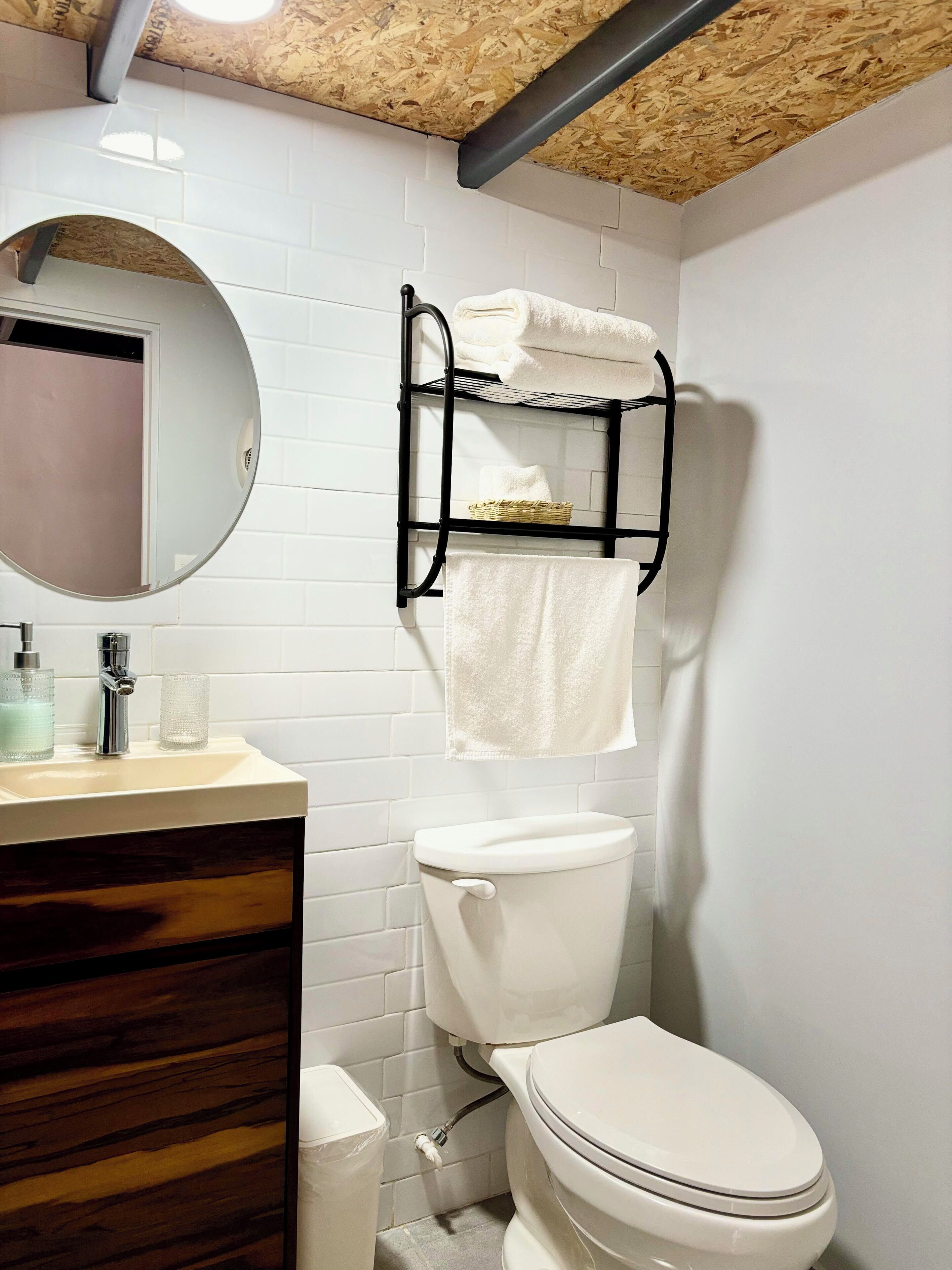 A bathroom with a toilet, sink, mirror, towel rack, and a trash bin.