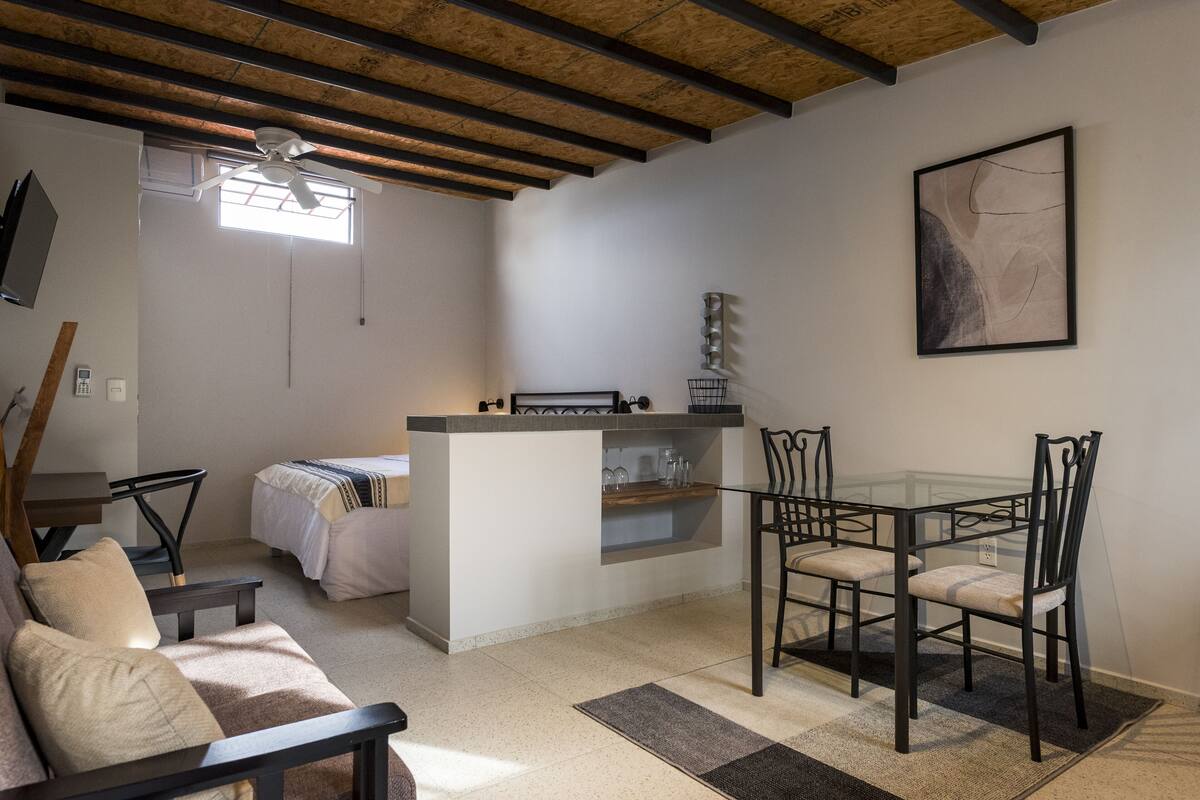 A compact living space with a kitchenette, a dining area with a glass table and chairs, a sofa, and a bed.