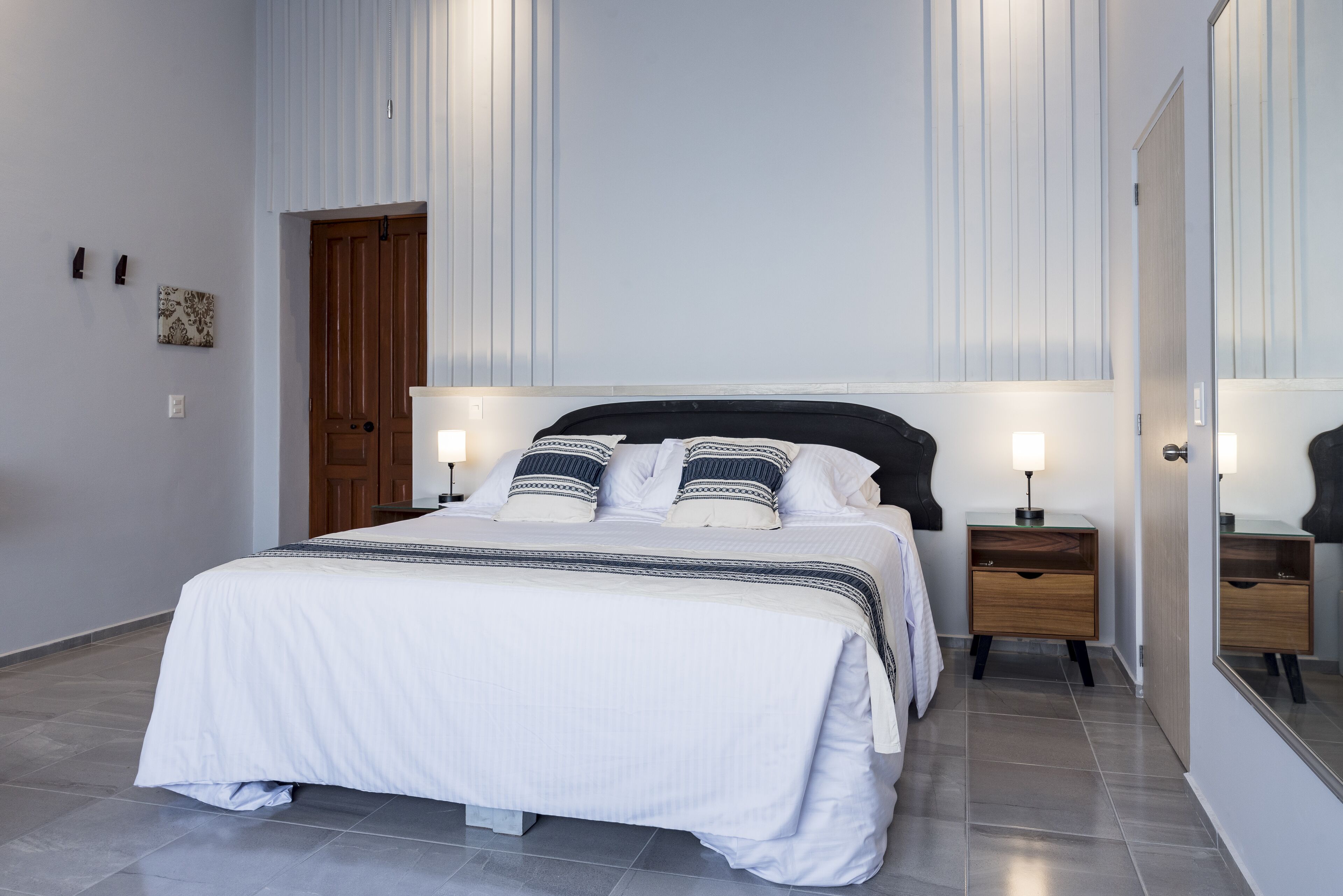 Ein ordentlich eingerichtetes Schlafzimmer mit Bett, Nachttischen und einem Spiegel.