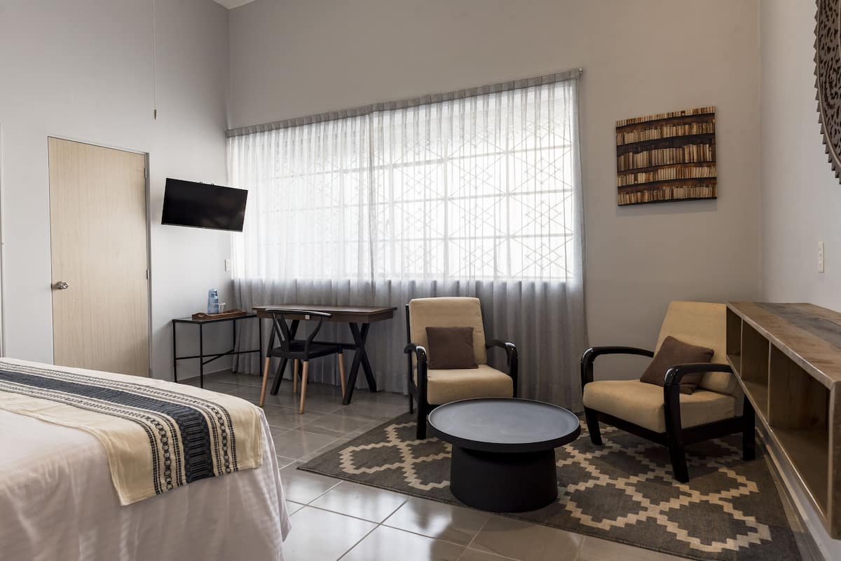 A hotel room with a bed, a desk, two chairs, a coffee table, a TV, and a bookshelf.