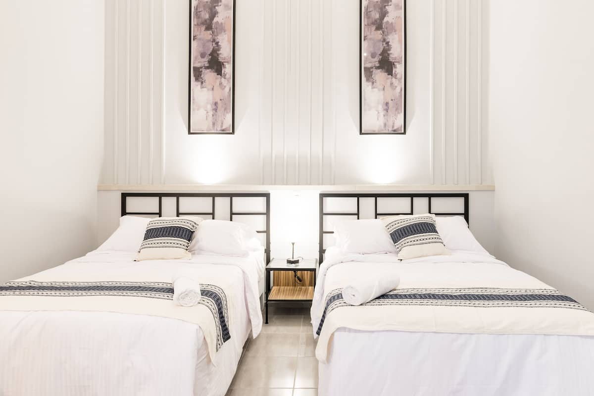 A hotel room with two beds, a nightstand, and a wall-mounted lamp.