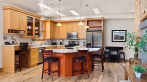 A modern kitchen with wooden cabinets, a central island with bar stools, stainless steel appliances, pendant lighting, and a dining area with a table and chairs. - Large Log Home Near Zion (Orderville)