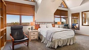 A bedroom with a large bed, a chair, a nightstand, and a window with a view of the desert. - Large Log Home Near Zion (Orderville)