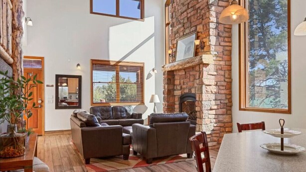 A spacious living room with a fireplace, a dining area, and a view of the outdoors. - Large Log Home Near Zion (Orderville)