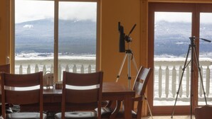 A dining area with a table and chairs, a telescope, and a balcony with a view of a snowy landscape. - Breathtaking Views Close to Yellowstone (Island Park)