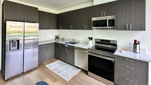 A modern kitchen with dark cabinets, stainless steel appliances, and a marble countertop. - Clean & stylish with exclusive patio, king bed, secured parking, by the beach  (San Diego)