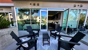 An outdoor patio with black chairs and a table, a glass door leading to a kitchen, and a view of the surrounding area. - Clean & stylish with exclusive patio, king bed, secured parking, by the beach  (San Diego)