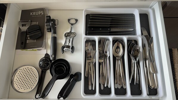 A drawer containing various kitchen utensils, including a grater, a can opener, and a set of knives and spoons.