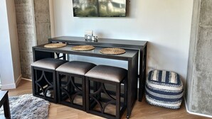 A dining area with a dark wooden table, three cushioned stools, a woven placemat, and a television mounted on the wall. - Clean & stylish with exclusive patio, king bed, secured parking, by the beach  (San Diego)