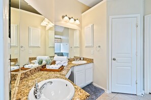 A bathroom with a large mirror, two sinks, a vanity, and a door.