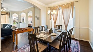 Un comedor con una mesa de madera dispuesta para seis personas, rodeada de sillas, y una mesa de futbolín al frente.