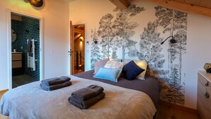 A bedroom with a bed, towels, a wall mural, and a wooden ceiling.
