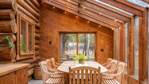 Un intérieur en bois avec une table ronde et six chaises, de grandes fenêtres et une vue sur l’extérieur.