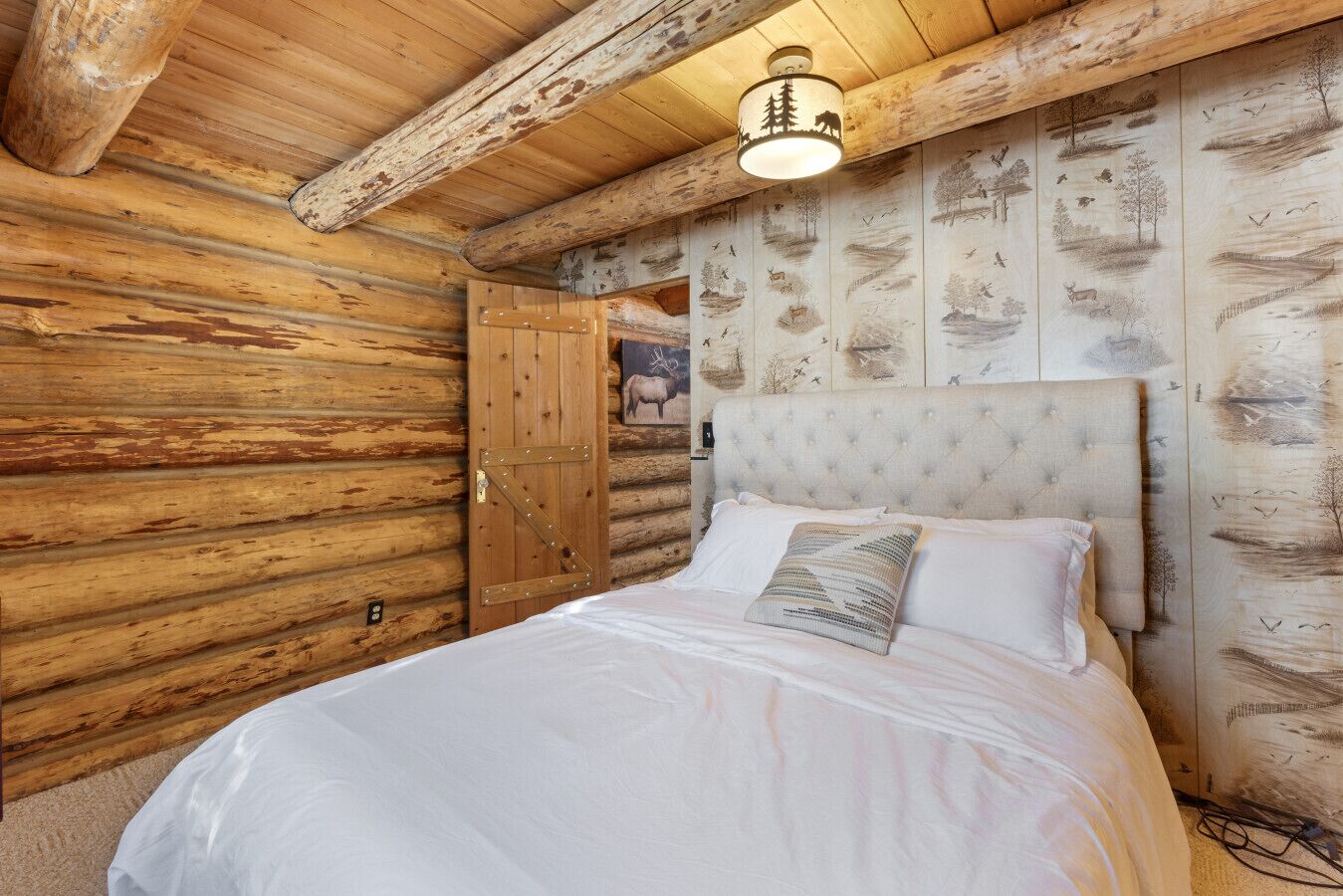 A log cabin bedroom with a bed, a wooden door, and a wall with painted scenes.