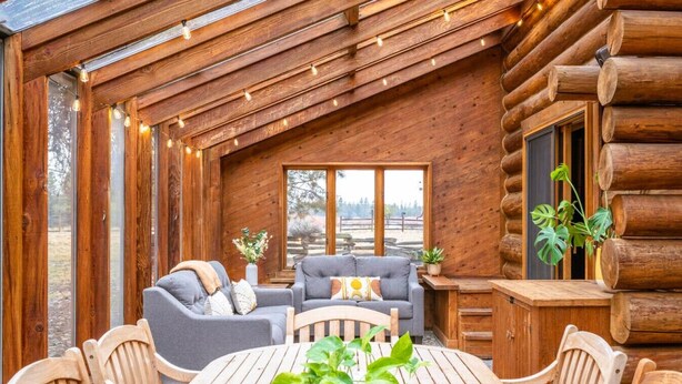 Une cabane en rondins dotée d’un intérieur chaleureux, avec un plafond en bois, une table à manger avec des chaises et un coin salon comprenant un canapé et des fauteuils.