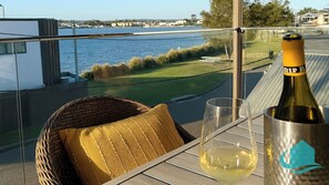 A balcony with a view of a body of water, a wicker chair, a glass, and a bottle of wine. - Village Bay Lake house, family Lake House with Spa (Marks Point)