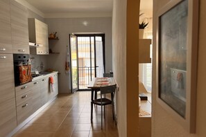 A modern kitchen with light wood cabinets, a dining area with a table and chairs, and a large window with a view of the outdoors.