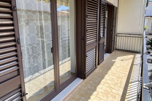 A balcony with sliding glass doors and shutters, a tiled floor, and a view of the street.