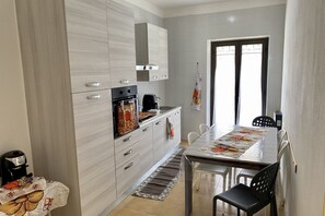 A modern kitchen with light wood cabinets, a built-in oven, and a dining area with a table and chairs.