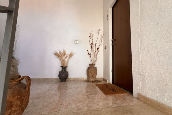A hallway with a tiled floor, a brown door, and two vases with dried plants.