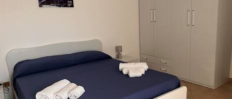 A neatly made bed with blue bedding and white towels, a bedside lamp, and a wardrobe with two doors.