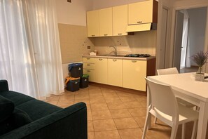 A compact kitchen with yellow cabinets, a white countertop, and a sink. There is a dining table with white chairs and a green sofa in the foreground.