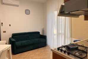 Cocina compacta con estufa a gas, sofá y un reloj en la pared.