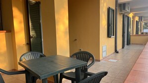 Ein überdachter Außenbereich mit Tisch und Stühlen, einer Tür und einem Fenster mit Fensterläden.