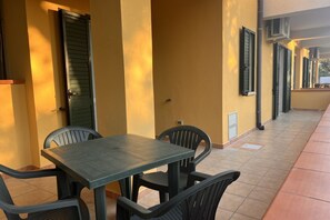 Un espacio de estar al aire libre cubierto con una mesa, sillas, una puerta y una ventana con contraventanas.