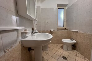 Un baño con lavamanos, bidé y ventana.