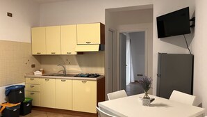 Une cuisine de taille réduite avec des meubles de couleur jaune, un évier et une cuisinière. On y trouve une table à manger avec des chaises et un téléviseur fixé au mur.