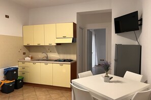 Eine kleine Küche mit gelben Schränken, einer Spüle und einem Herd. Ein Esstisch mit Stühlen und ein an der Wand befestigter Fernseher sind ebenfalls vorhanden.