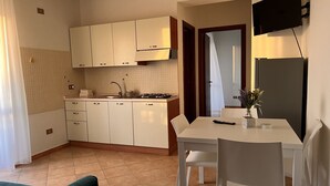 Une cuisine compacte avec des meubles blancs, une cuisinière à gaz et un coin repas comprenant une table et des chaises.