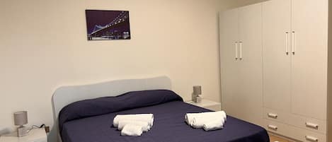 Un dormitorio con cama, dos mesitas de noche, un armario y un cuadro enmarcado en la pared.