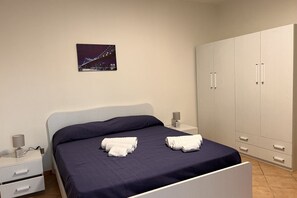 Ein Schlafzimmer mit einem Bett, zwei Nachttischen, einem Kleiderschrank und einem gerahmten Bild an der Wand.