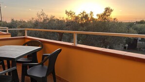 Un balcon avec une table et des chaises, donnant sur un paysage arboré et un coucher de soleil.