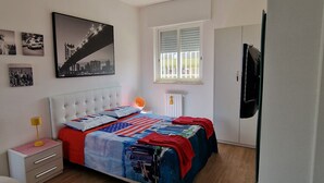 A bedroom with a bed, a nightstand, a lamp, a radiator, a window with blinds, and a wall with framed pictures. - Special Guest Home (BARI)