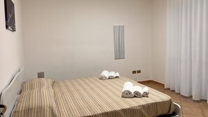 A hotel room with a single bed, a small bedside table, a wall-mounted TV, and a window with curtains.
