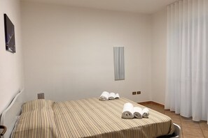 Habitación de hotel con una cama individual, una mesita de noche pequeña, un televisor montado en la pared y una ventana con cortinas.