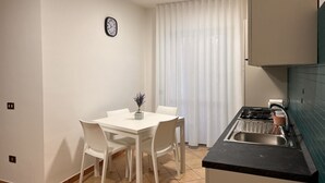A compact kitchen with a dining table and chairs, a sink, and a clock on the wall.