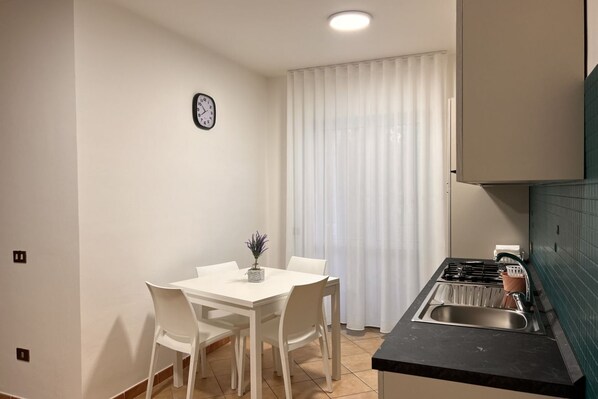 A compact kitchen with a dining table and chairs, a sink, and a clock on the wall.