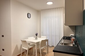 A compact kitchen with a dining table and chairs, a sink, and a clock on the wall.