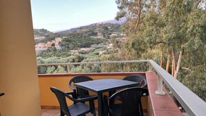 A balcony with a table and chairs, overlooking a hillside with buildings.