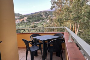 Ein Balkon mit Tisch und Stühlen mit Blick auf eine Hügellandschaft und Gebäude.