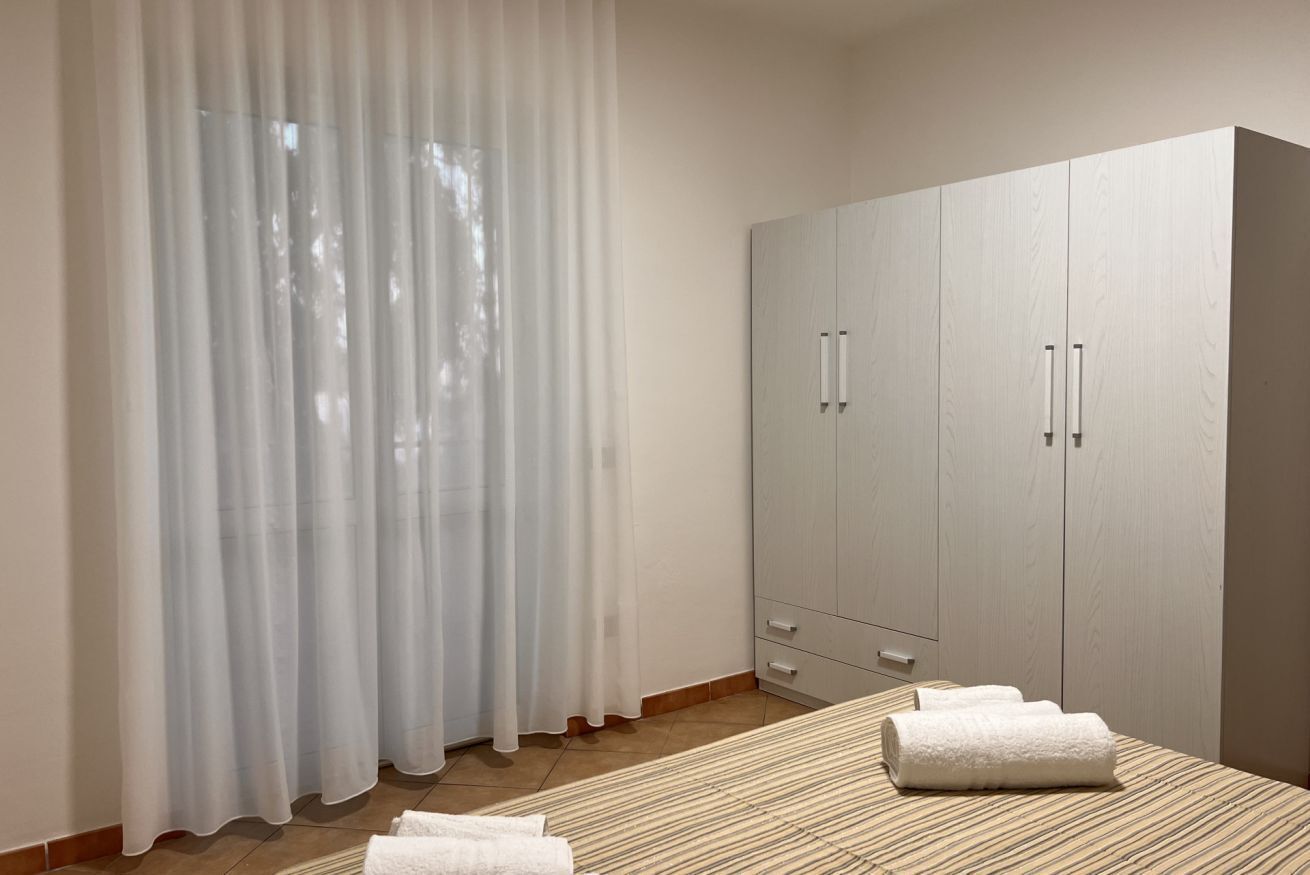 A bedroom with a bed, a wardrobe, and a window with sheer curtains.