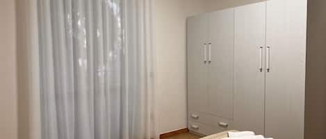 A bedroom with a bed, a wardrobe, and a window with sheer curtains.