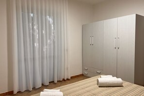 A bedroom with a bed, a wardrobe, and a window with sheer curtains.