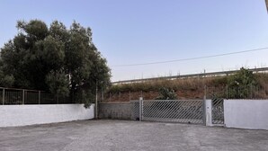 Un espace de stationnement extérieur doté d’une entrée fermée par un portail, d’un grand arbre et d’une clôture.