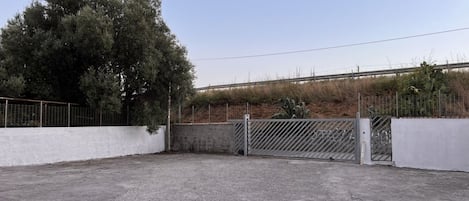 An outdoor parking area with a gated entrance, a large tree, and a fence.